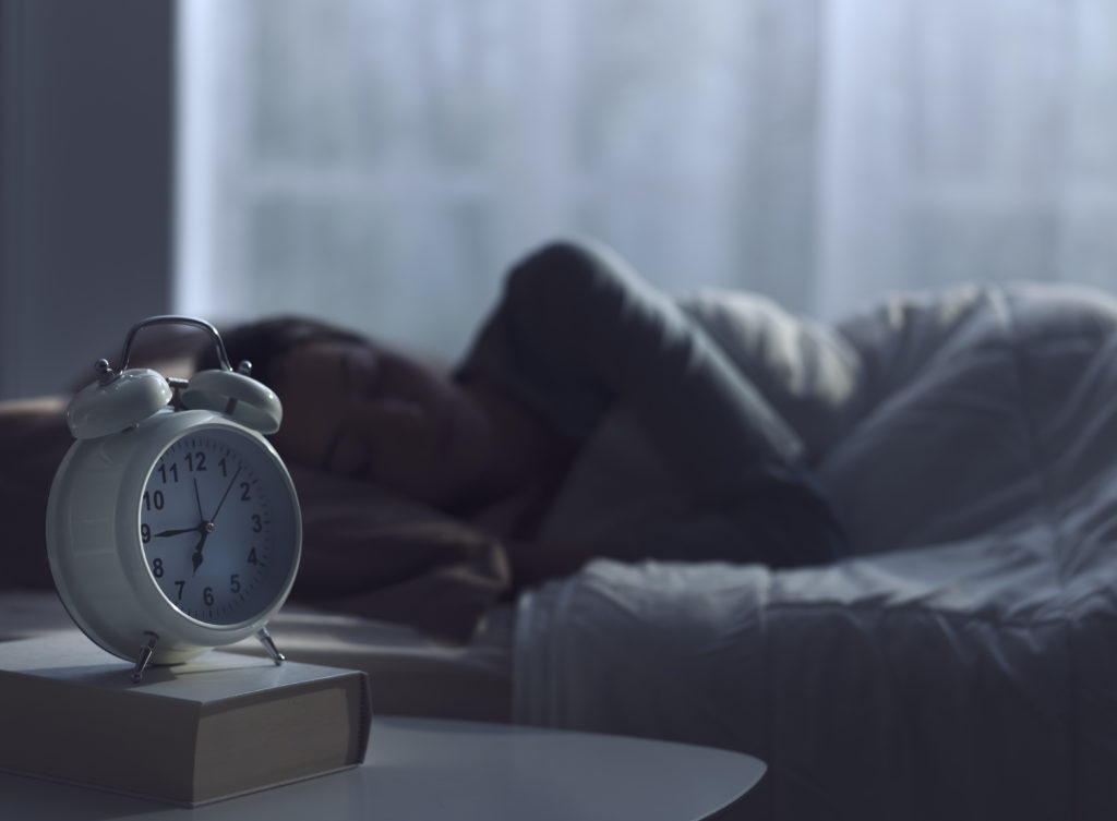 Person sleeping in bed and alarm clock in the foreground